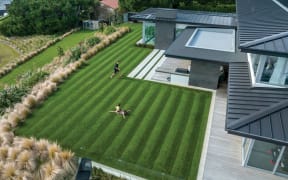 A perfectly striped lawn next to a grey and glass house. Children play on the lawn.