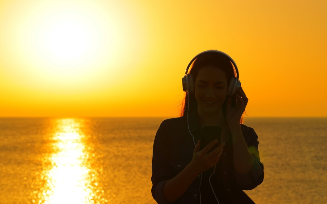 Front view of a woman silhouette listening to music at sunset on the beach