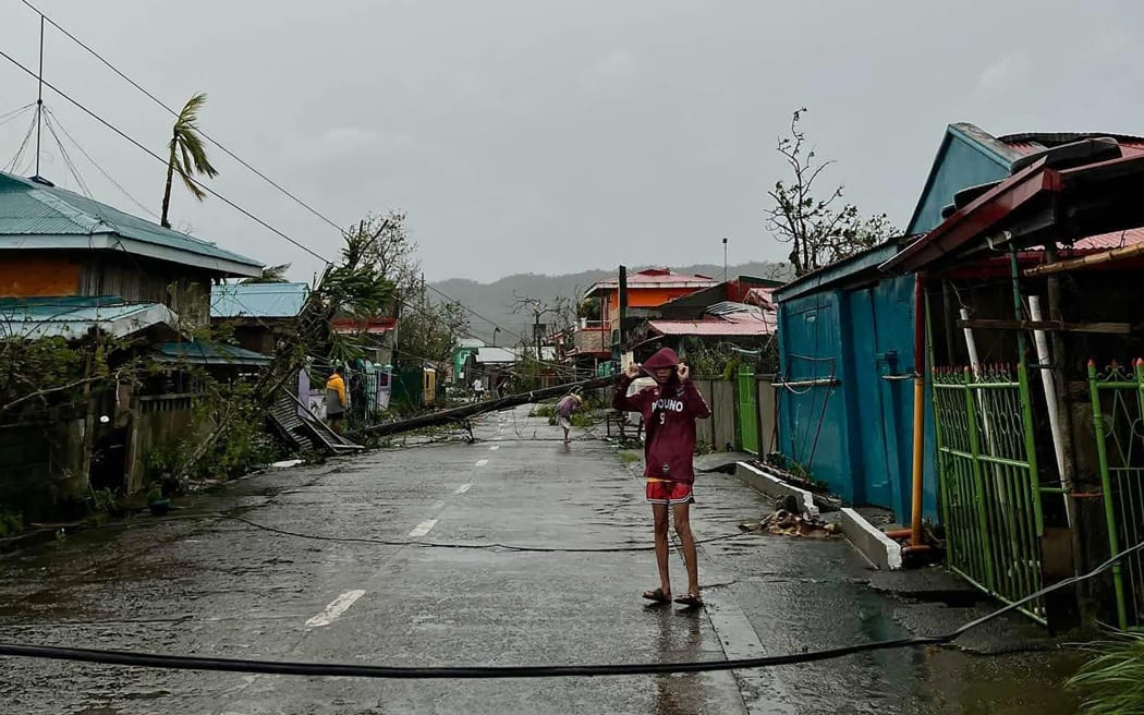 This handout taken and released on November 17, 2024 courtesy of Mayor Cesar Robles shows a resident standing past an uprooted electric post (background) in Panganiban town, Catanduanes province, after Super Typhoon Man-yi hit the province. - Super Typhoon Man-yi slammed into the Philippines' most populous island on November 17, with the national weather service warning of flooding, landslides and huge waves as the storm sweeps across the archipelago nation. (Photo by Handout / Mayor Cesar Robles / AFP) / -----EDITORS NOTE --- RESTRICTED TO EDITORIAL USE - MANDATORY CREDIT "AFP PHOTO / COURTESY OF MAYOR CESAR ROBLES" - NO MARKETING - NO ADVERTISING CAMPAIGNS - DISTRIBUTED AS A SERVICE TO CLIENTS