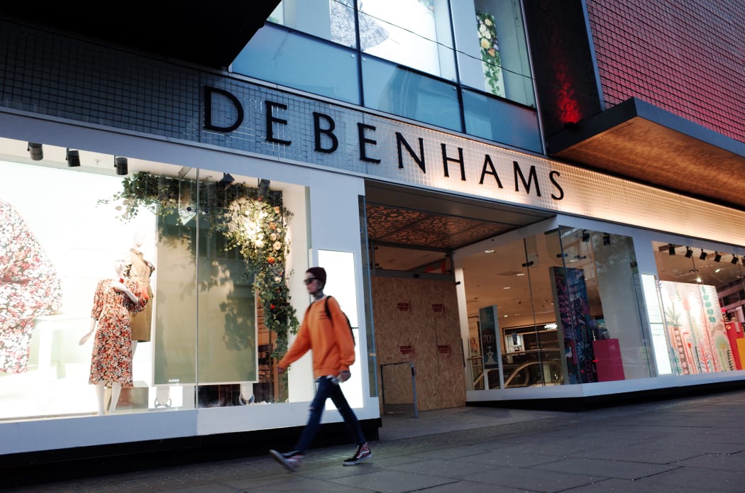 A woman walks past the boarded-up flagship branch of department store chain Debenhams on a near-deserted Oxford Street in London, England, April 2020.