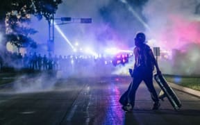 A demonstrator carries a makeshift shield across the street in Kenosha, Wisconsin, 25 August 2020.