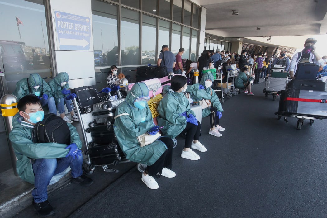 Passengers in protective gear sit on the pavement as they wait for their flights out of the country at Manila's international airport on March 19, 2020.