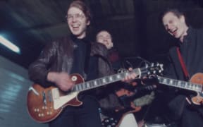 Four young men holding musical instruments laugh together.