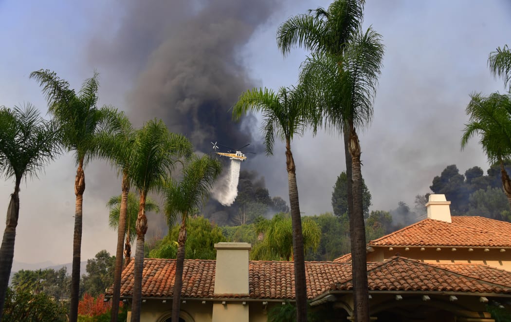 A helicopter drops water on fires threatening homes in Bel Air.