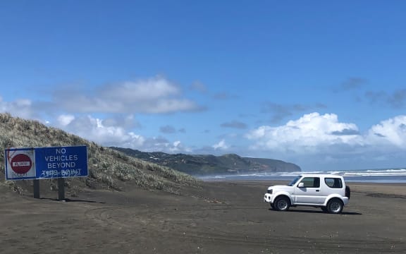 A white four-wheel driving is parked near a sign saying 'no vehicles beyond this point' on Muriwai Beach
