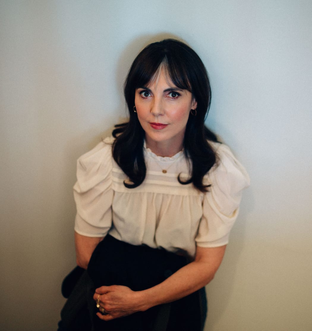 Author Emily Perkins sitting wearing a cream coloured blouse and black skirt.