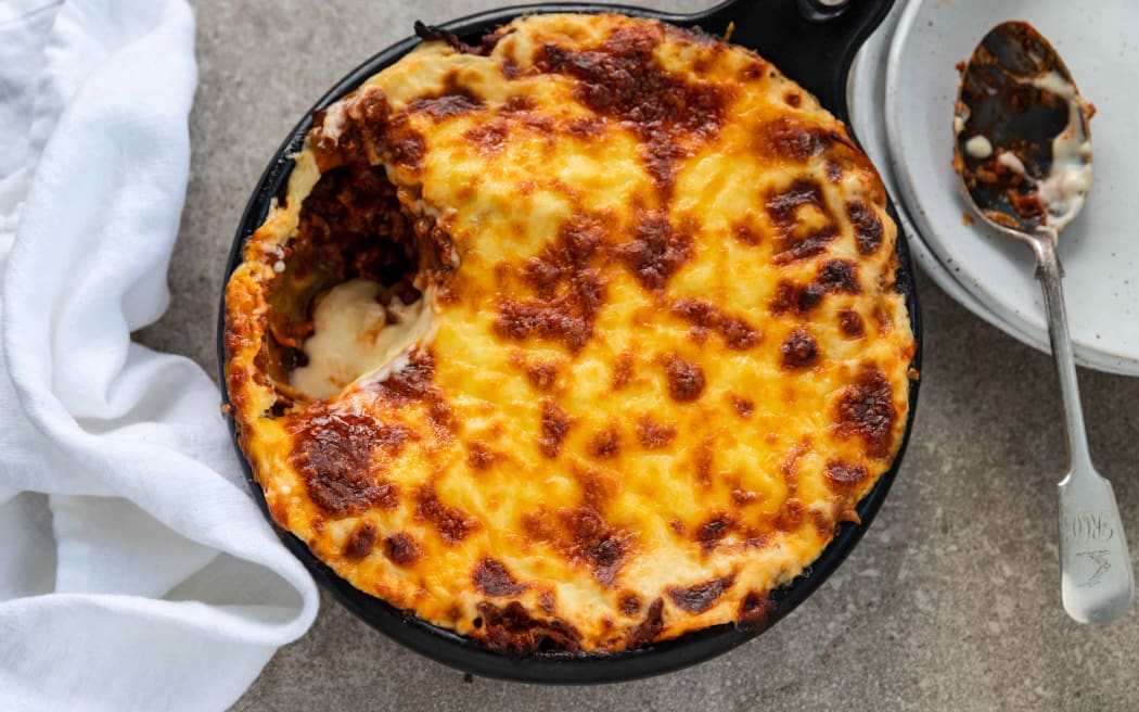 A round dish of lamb lasagne covered with a baked cheese topping.