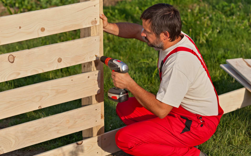 Man building a wooden fence - fastening the boards with screws