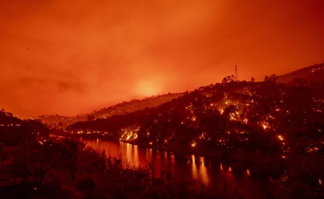 In this long exposure photograph, flames set ablaze both sides of a segment of Lake Berryessa during the Hennessey fire in the Spanish Flat area of Napa, California on 18 August, 2020.