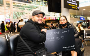 People waiting at Auckland Airport hold a 'welcome' sign as they wait for passengers to disembark from first flight from Sydney to Auckland under the trans-Tasman bubble arrangement.