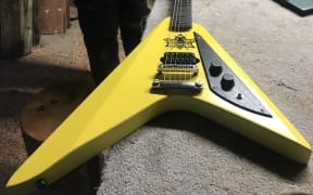 A bright yellow guitar laid out in a dark workshop, an insect decal featured on the center of the guitar.