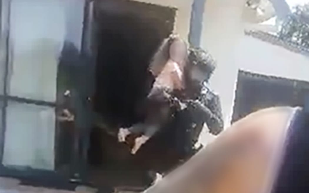 Still from video showing an armed offender squad policeman rescuing a girl from a house in Tauranga 24 November 2019 after a man had been shot by police during a hostage situation at the address