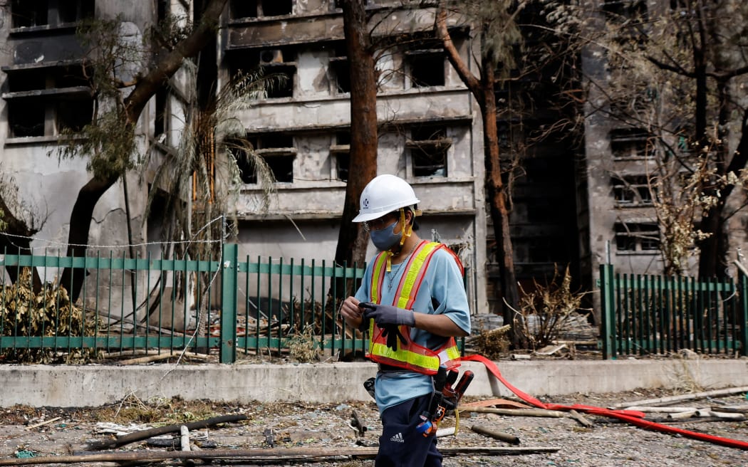 A repair worker walks past burnt buildings after the deadly fire at the Wang Fuk Court housing complex, in Tai Po, Hong Kong, on November 29, 2025.