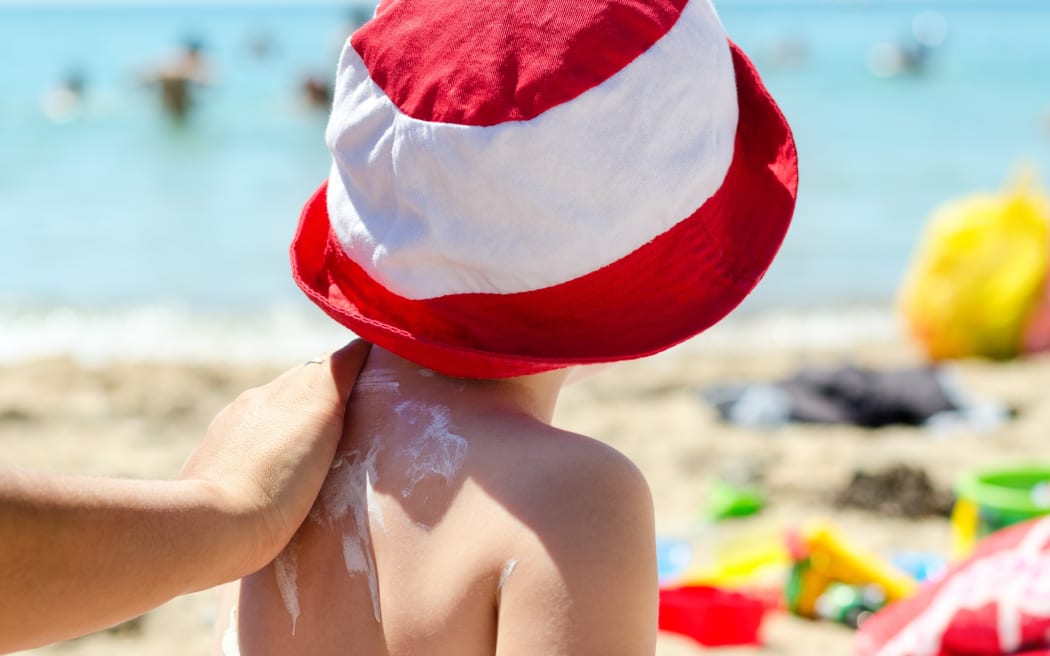 Child on the beach putting sunscreen.