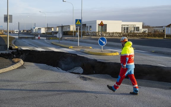 This photo taken on November 13, 2023 shows a member of the emergency services walking near a crack cutting across the main road in Grindavik, southwestern Iceland following earthquakes. The southwestern town of Grindavik -- home to around 4,000 people -- was evacuated in the early hours of November 11 after magma shifting under the Earth's crust caused hundreds of earthquakes in what experts warned could be a precursor to a volcanic eruption.  The seismic activity damaged roads and buildings in the town situated 40 kilometres (25 miles) southwest of the capital Reykjavik, an AFP journalist saw. (Photo by Kjartan TORBJOERNSSON / AFP) / Iceland OUT