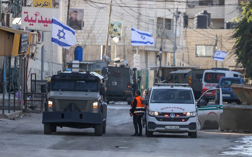 Israeli forces in armoured vehicles stop a Palestinian ambulance for a search as they block a road during a raid in Jenin in the occupied West Bank on 21 January 2025.