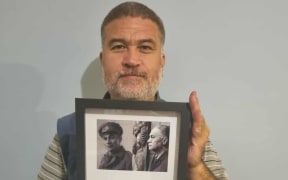 Albert Tibble holding a plaque with information about his Tipuna Te Rauwhiro Tibble who received a Military Cross for bravery.
