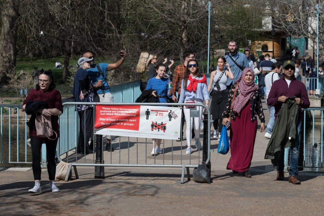 LONDON, UNITED KINGDOM - MARCH 30, 2021: People walk past a social distancing banner during exceptionally warm and sunny weather in St James's Park, making the most of eased Coronavirus restrictions, on 30 March, 2021 in London, England.
