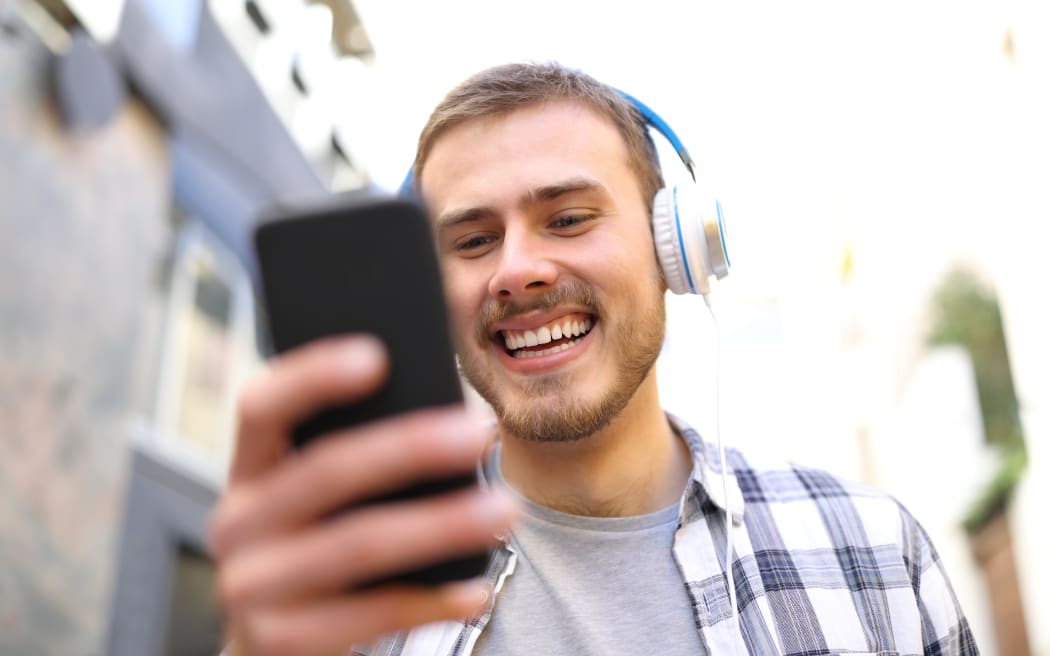 Portrait of a happy man listening to the music with smart phone walking in the street