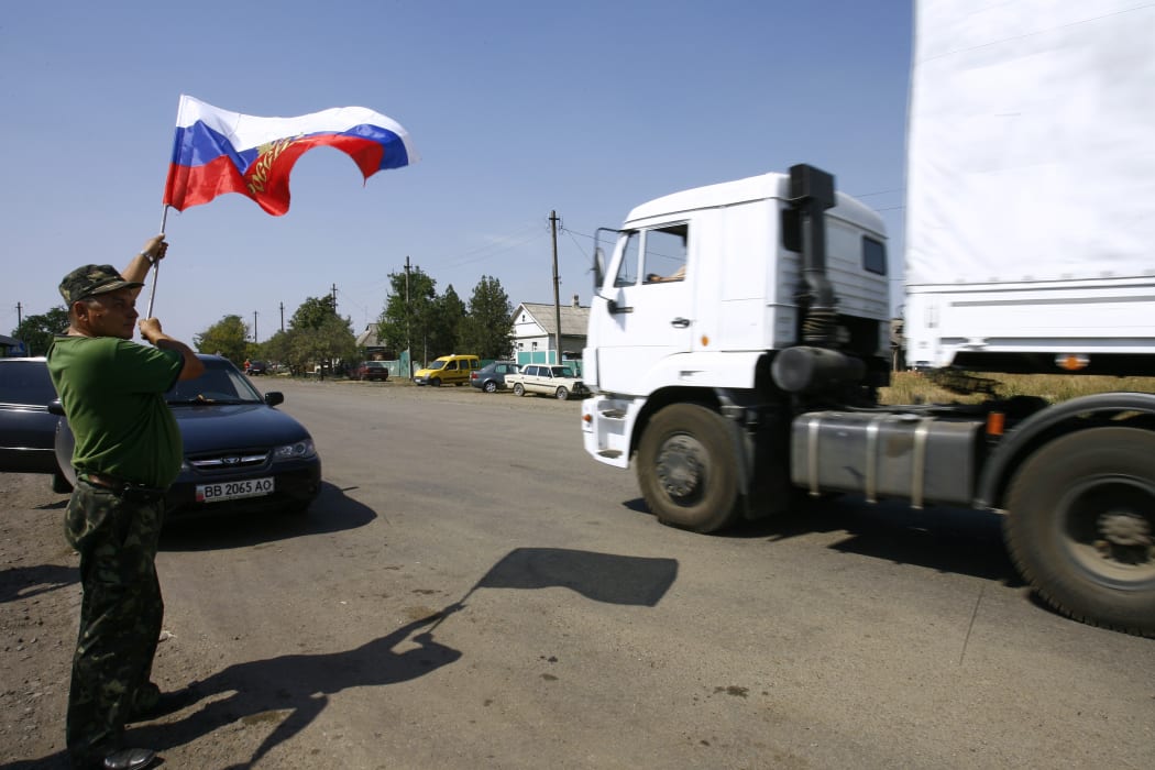 A local resident holds a Russian national flag as lorries, part of a Russian humanitarian convoy, cross the Ukrainian border on August 22, 2014.