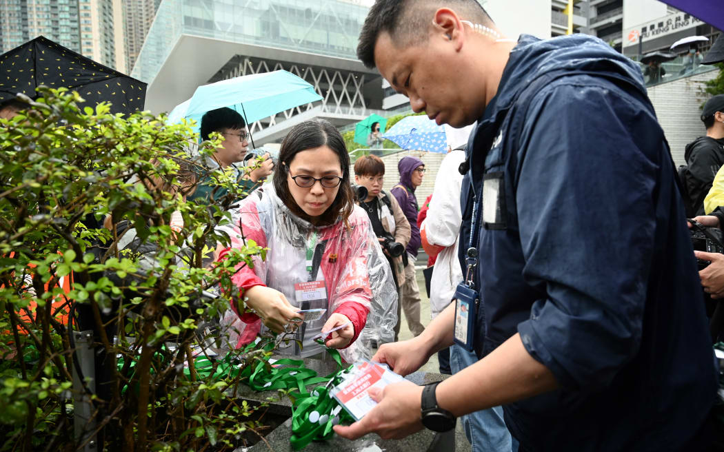 A police officer issues numbered lanyards to protesters to a group of residents to have to wear as they hold the first authorised protest and march in several years in Hong Kong against the proposal for reclamation in the district on Tseung Kwan O on 26 March, 2023.
