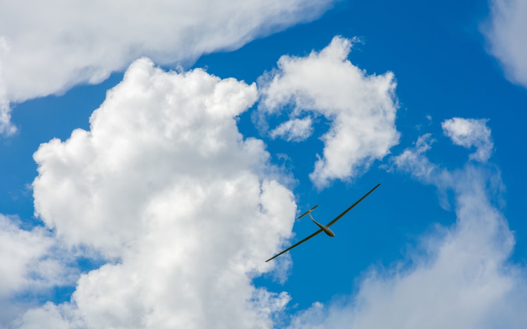 A Glider flying in bleu sky with big white clouds. The glider is a plane that has no engine