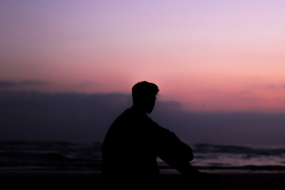 A young person with short hair looks into the sunset.