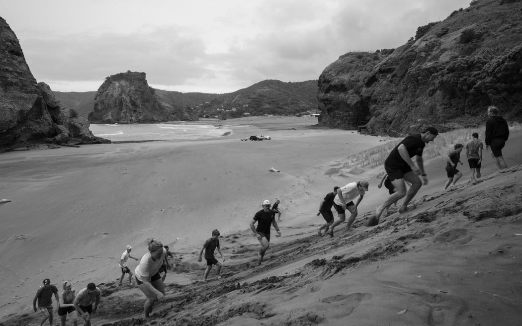 People struggling to run up a sand dune.