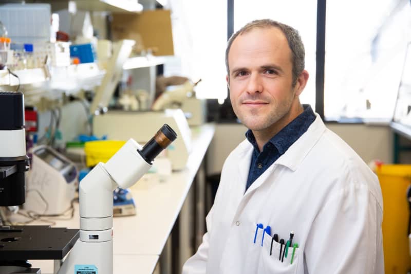 Dr. Victor Dieriks sits in a lab with a lab coat on in front of a microscope.