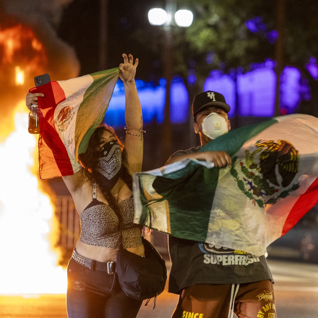Protesters hold up Mexican flags amid clashes with law enforcement in the streets surrounding the federal building during a protest following federal immigration operations in Los Angeles, California, on June 8, 2025. Demonstrators torched cars and scuffled with security forces in Los Angeles on June 8, as police kept protestors away from the National Guard troops President Donald Trump sent to the streets of the second biggest US city. (Photo by RINGO CHIU / AFP)