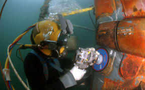 Navy diver using an angle grinder underwater on a segment of piping