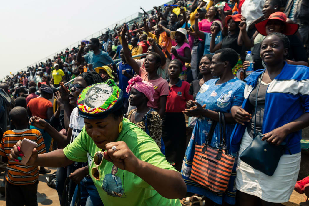 A lady wearing a Robert Mugabe cap dances as people gather for viewing the body of Robert Mugabe lying in state during a public send off at the Rufaro Stadium in Harare on September 13, 2019.