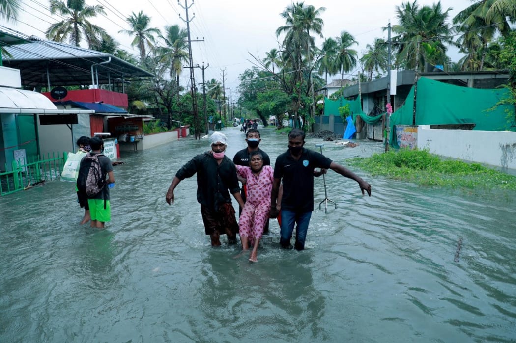 Police and rescue personnel evacuate a local resident through a flooded street in a coastal area after heavy rains under the influence of cyclone 'Tauktae' in Kochi on May 14, 2021.