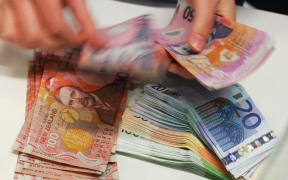 A currency exchange teller counts out New Zealand dollars alongside a stack of Euros in Auckland, 21 April 2007. The New Zealand dollar hit 74.91 US cents on18 April, the highest level since 1982 and a record since the currency was floated in 1985. On 19 April the currency opened local trading at 74.70 US cents.   AFP PHOTO/Dean TREML (Photo by DEAN TREML / AFP)