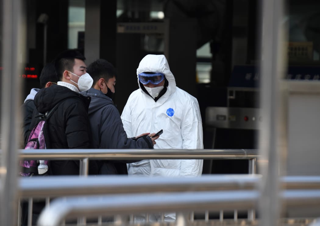 Passengers wearing protective facemasks are checked by security personnel wearing hazardous material suits at the entrance to the underground train station in Beijing on January 24, 2020, to help stop the spread of a deadly SARS-like virus which originated in the central city of Wuhan.