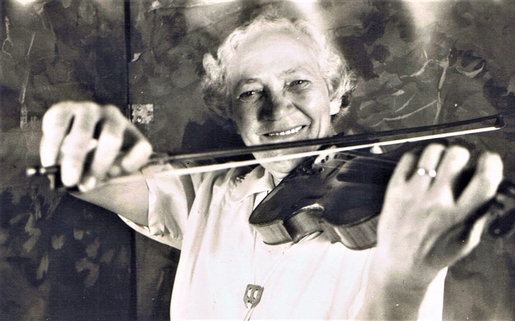 Woman smiles at camera while playing the violin.