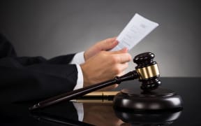 Close-up Of Judge Holding Document With Gavel At Desk