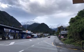 A view of the main street of Franz Josef, with snowy mountains in the background.