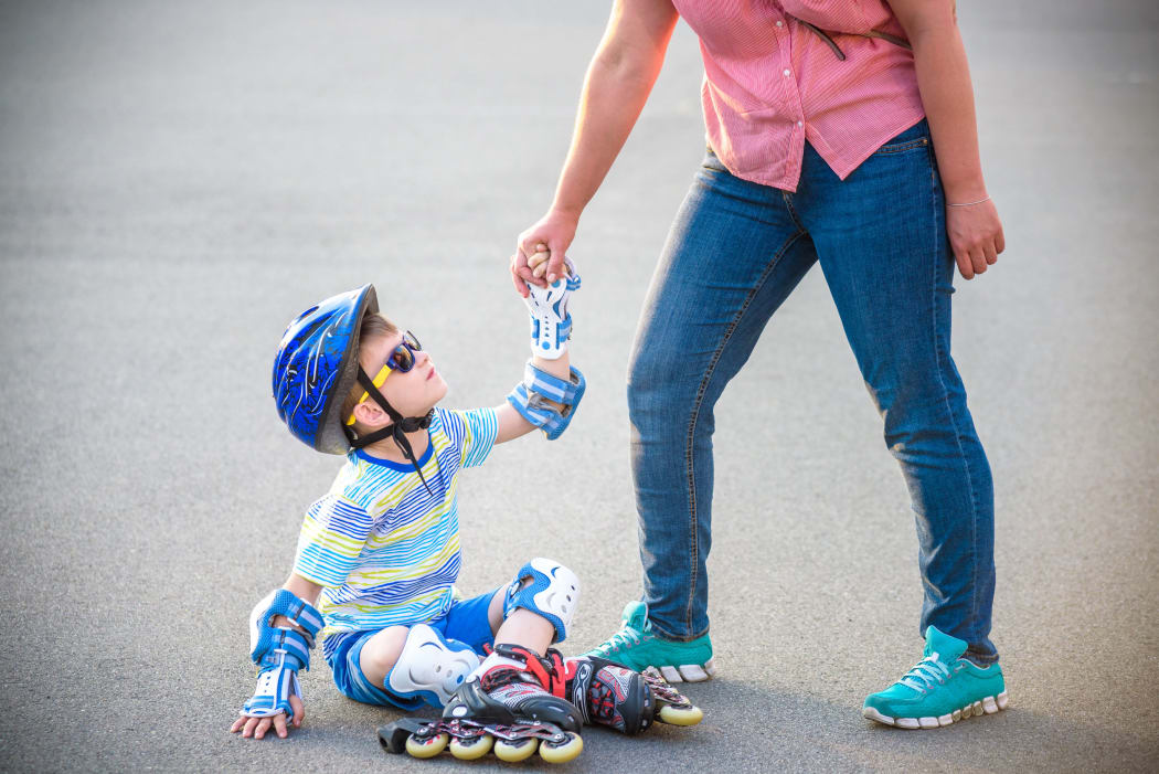 A photo of a Preschooler falling over while rollerblading with mother in the park.
