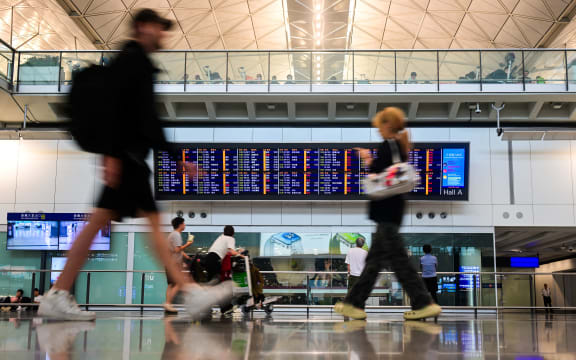 Passengers walk past a flight information board at the Hong Kong International Airport.