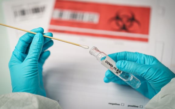 Hand holding COVID-19 swab collection kit, specimen sample testing process.