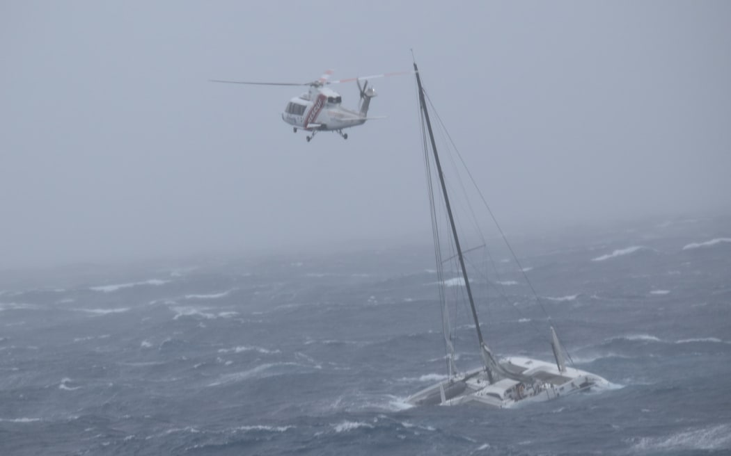 A catamaran that drifted out to sea in strong winds can be seen in the water with a helicopter flying above.