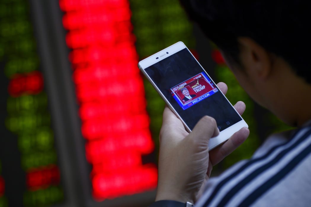 An investor looks at his smartphone showing results from the US presidential election, at a securities company in Beijing on November 9, 2016