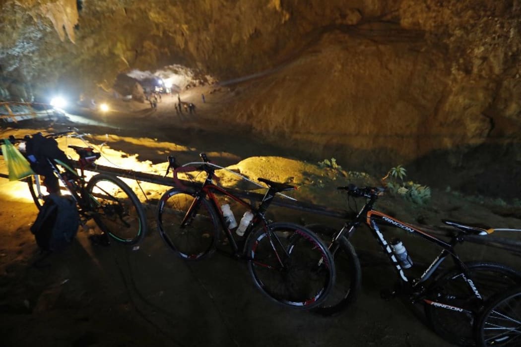 Bicycles belonging to members of a children's football team, who are trapped in a cave chamber along with their coach, are seen as Thai rescue personnel (background) conduct operations under floodlights at the entrance to Tham Luang cave at the Khun Nam Nang Non Forest Park in Chiang Rai.