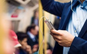 A man wearing headphones uses his smartphone on a train.