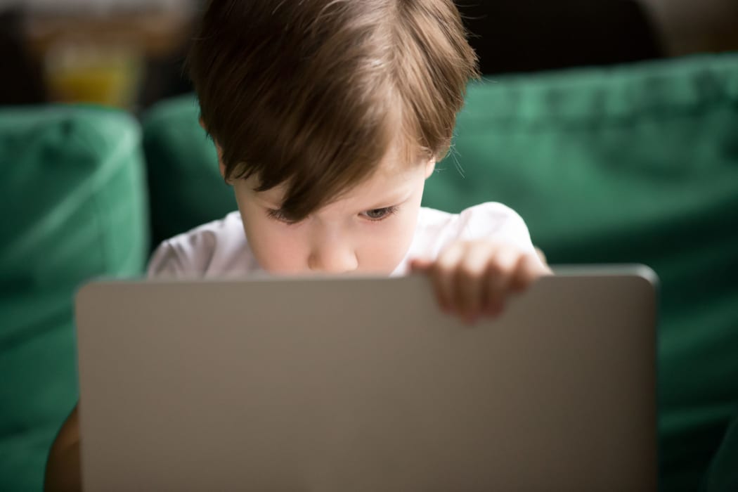 A photo of a Curious interested kid boy secretly looking watching forbidden censored adult only internet online video content on laptop alone, parental protection, computer control and security for child concept