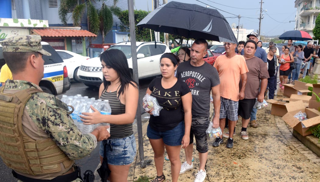 A Coast Guard member deployed to Borinquen, Puerto Rico in support  of Hurricane Maria relief efforts delivers a case of water to a resident of Moca, Puerto Rico, Oct. 9, 2017.