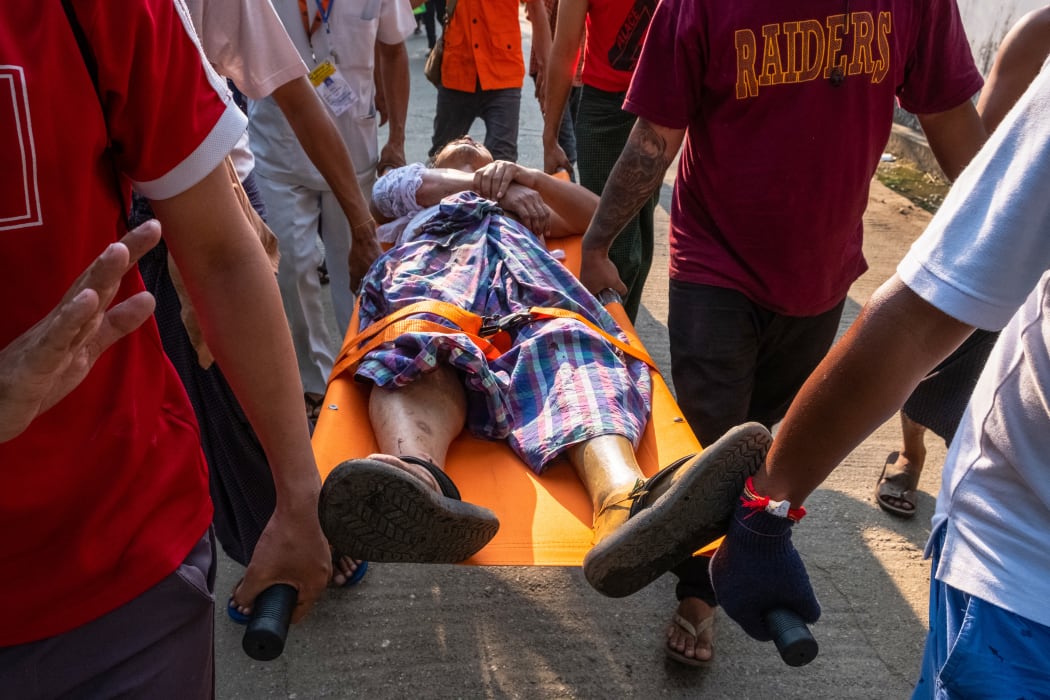 People carry an injured resident, who was shot with rubber bullets as security force destroyed barricades erected by protesters against the military coup in Yangon.