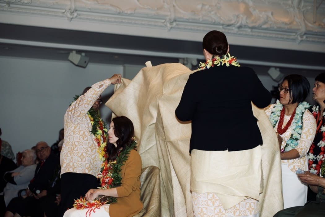 A mat is draped over Prime Minister Jacinda Ardern as part of the Samoan Ifoga ceremonial apology.