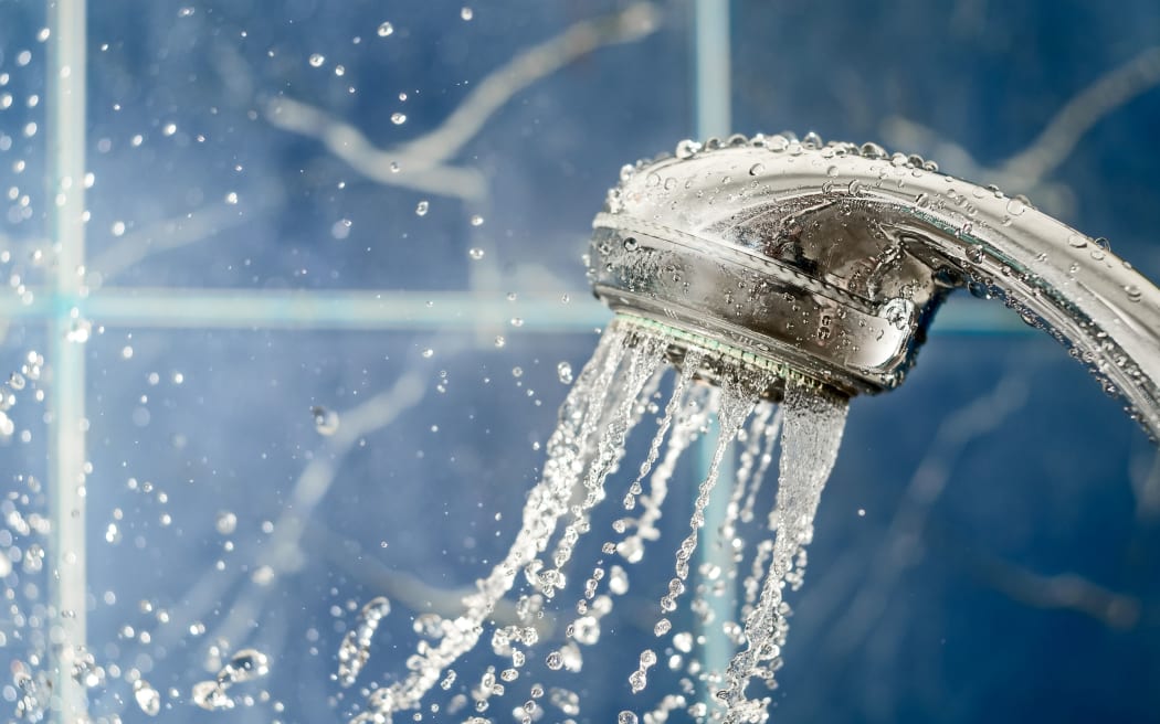 Showerhead with flow of water spilling out on blue background